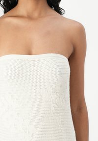 Off-white stickad strapless topp med en öppen vävstruktur och subtila bladmönster. Slät, elastisk material formar sig efter kroppen.