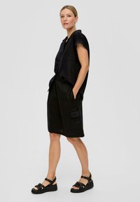 Chemise en lin noire à manches courtes, fermeture par boutons sur le devant, assortie à une jupe en lin noire avec poches latérales et coupe décontractée. Sandales noires.