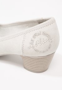 Chaussure à talon moyen en cuir suede gris avec un détail de logo embossé, présentant un bout rond et un talon rayé texturé pour une meilleure adhérence.