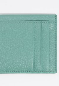 Tarjetero de cuero verde menta que cuenta con cuatro ranuras para tarjetas, superficie texturizada y costuras en contraste a lo largo de los bordes.