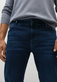 Dark blue denim jeans with a slim fit, front pockets, and a button closure. The fabric has a slight sheen and subtle texture.