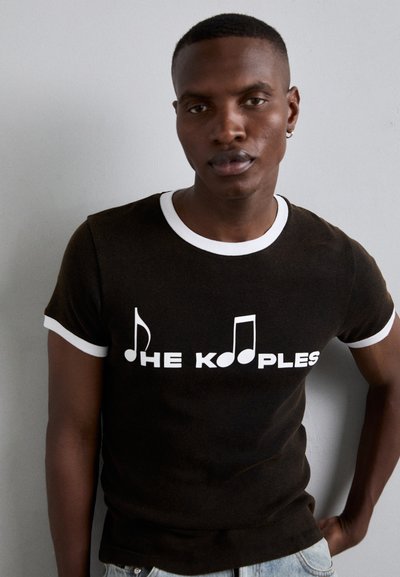 Crna majica kratkih rukava s bijelim obrubom i grafičkim tekstom "THE KOOPLES" te notama, izrađena od glatkog materijala.