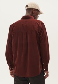 Donkergroene corduroy-overhemd met een relaxte pasvorm, lange mouwen, knopenmanchetten en een rugpaneel detail. Het ontwerp heeft een zachte textuur.
