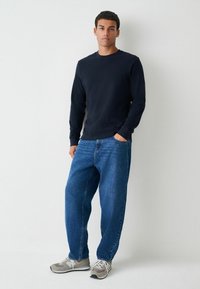 Marineblauw shirt met lange mouwen, losse blauwe jeans en grijze sneakers. Glad katoen, relaxte pasvorm en een minimistisch ontwerp zonder patronen.