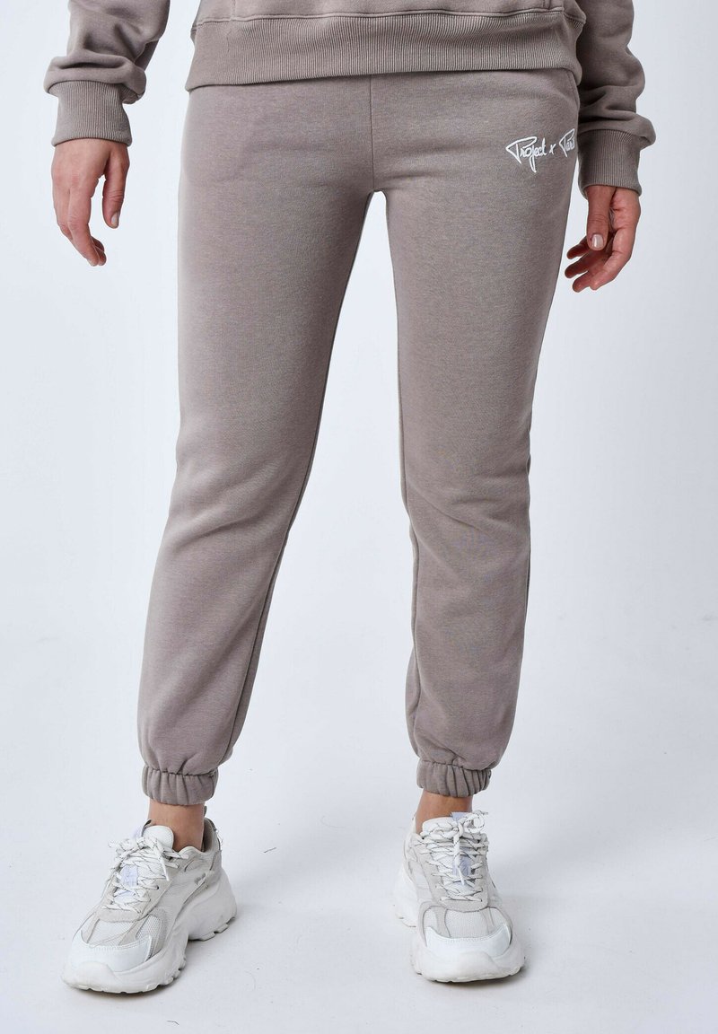 Grijze joggingbroek van zacht materiaal, met elastische boorden, een getailleerd ontwerp en een wit logo detail op de linker bovenbeen.