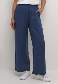 Navy blue wide-leg pants made of lightweight fabric, featuring an elastic waistband and side pockets, styled with white sneakers.