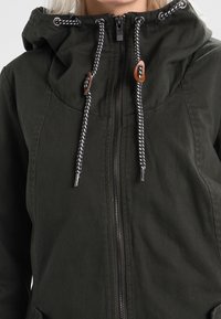 Veste à capuche vert foncé avec fermeture éclair à l'avant et cordons noirs et blancs avec boutons en bois.