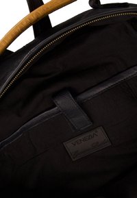 Czarna skórzana torba od wewnątrz o gładkiej fakturze, z suwakiem i skórzaną metką oznaczoną "VENEZIA Genuine Leather". Jasnobrązowy uchwyt.