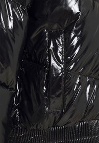 Černá péřová bunda s lesklou texturou, prošívaným designem a elastickým pasem. Má boční kapsu a kontrastní švy.
