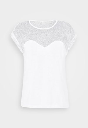 Blouse blanche à manches courtes avec empiècement et manches en dentelle transparente, présentant un décolleté en cœur sous le détail en dentelle.