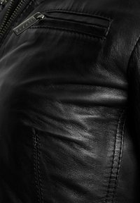 Primo piano di una giacca in pelle nera che mostra la superficie testurizzata, i dettagli delle cuciture e una cerniera con il marchio "bugatti".