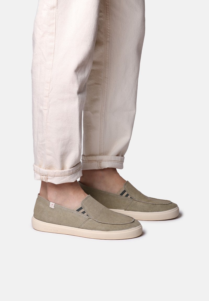 Grønne slip-on sko lavet af lærred med elastiske detaljer i siderne og en gummisål, kombineret med opsmøgede lyse beige bukser.