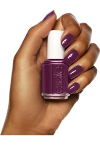 Bottiglia di smalto per unghie viola con tappo bianco tenuta in una mano, unghie smaltate di un elegante viola lucido. Texture liscia con etichettatura chiara.