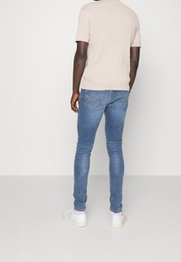 Camisa de manga corta de punto en color beige con un acabado texturizado, combinada con jeans ajustados azules que cuentan con bolsillos traseros y costuras de un tono beige claro.