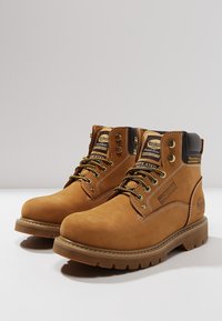 Botas de trabajo aisladas de color marrón, hechas de ante, con un diseño de cordones, cuello acolchado, detalles de costura y una suela de goma gruesa.