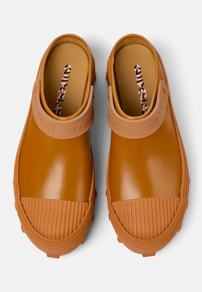 Brown rubber clogs with a textured strap and ridged toe. Smooth surface with a patterned insole. Slightly raised heel and durable sole.