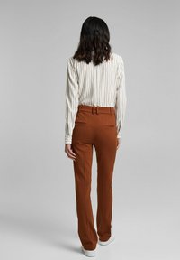 Hnědé upravené kalhoty s rovnými nohavicemi, vyrobené z hladké tkaniny. V kombinaci s bílou pruhovanou košilí s dlouhým rukávem. Bez viditelných vzorů.