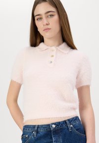 Šviesiai rožinė, trumpomis rankovėmis polo megztinis, pagamintas iš pūkuoto audinio, su apykakle ir trimis sagomis priekyje. Minkšta tekstūra.