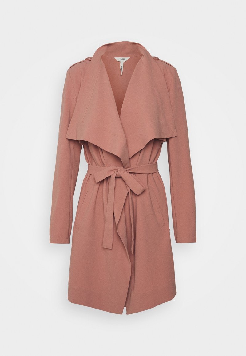 Trench-coat ceinturé rose poudré à manches longues avec larges revers et épaulettes, suspendu sur un fond blanc.