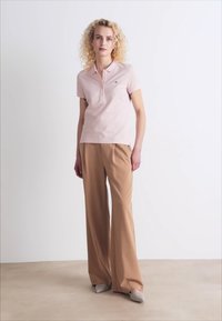 Lys rosa polo skjorte med krage, kombinert med skræddersydde beigefargede vide bukser. Mykt stoff, enkelt design og lysegrå slip-on sko.