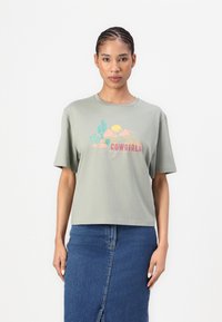 Gray cotton T-shirt with short sleeves, featuring colorful graphic of cacti and clouds, labeled "COWGIRLS," paired with a denim skirt.
