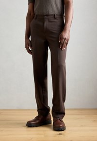 Pantalon sur mesure marron avec une coupe droite, doté de poches latérales, d'une fermeture à bouton et d'une texture lisse, assorti à des chaussures en cuir marron.