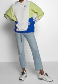 Felpa con cappuccio Nike a blocchi di colore in grigio, verde lime e blu. Presenta un orlo con coulisse e una tasca a marsupio. Abbinala a jeans azzurri e scarpe sportive.