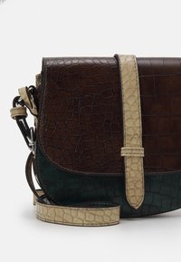 Brązowa i zielona skórzana torba na ramię z teksturowanym wzorem krokodylej skóry, beżowym paskiem i zakrzywionym klapką. Widoczne szczegóły metalowych elementów.