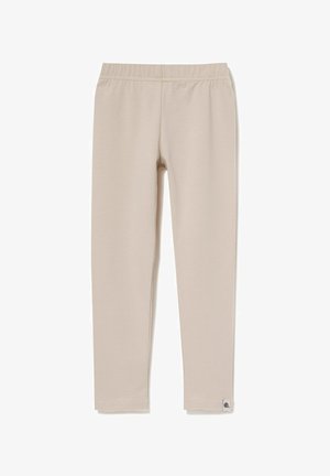 Beżowe legginsy wykonane z miękkiego materiału, z elastycznym pasem i małą metką z logo u dołu nogawki. Długa, dopasowana sylwetka.