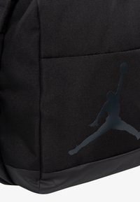Mochila negra hecha de tela texturizada con un gran logo gris de Jumpman en el costado y una costura inferior suave.