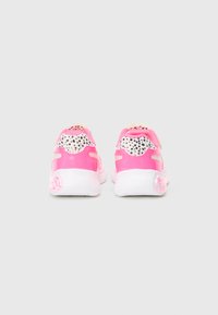 Zapatillas deportivas rosas con un acabado brillante, diseño de manchas en el talón, suelas blancas y una correa de velcro para un ajuste seguro.