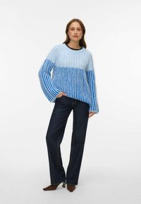 Hele sinine ülisuur kampsun tekstuursete mustritega, millel on laiad triibulised varrukad. Kombineeritud tumeliste teksapükstega.