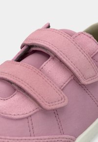 Lyserøde sneakers lavet af blødt suede med to velcro-stropper. Har rund tå, stikninger og en hvid gummisål.