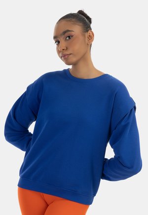 Modrá mikina s uvolněným střihem, kulatým výstřihem a oversized rukávy. Vyrobena z hladké látky, s žebrovanými manžetami a spodním lemem.