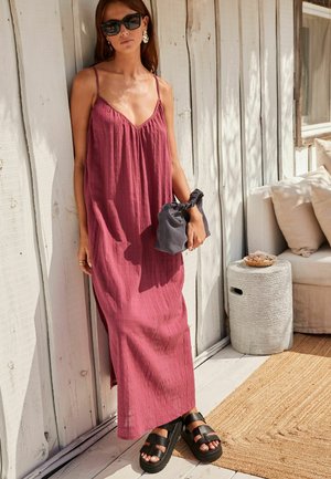 Maxikjole i dyb pink stof med en tekstureret finish, som har tynde stropper og en løs pasform. Sorte platform sandaler og en mørk håndtaske holdes.