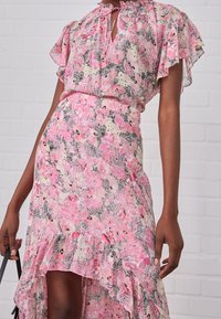 Vestido floral rosa con dobladillo con volantes y mangas cortas con vuelo. Presenta un cierre con lazo en el cuello y una cintura ajustada, hecho de tela ligera.