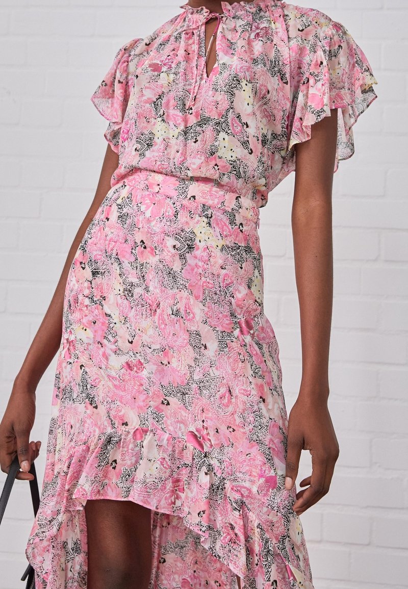 Vestido floral rosa con dobladillo con volantes y mangas cortas con vuelo. Presenta un cierre con lazo en el cuello y una cintura ajustada, hecho de tela ligera.