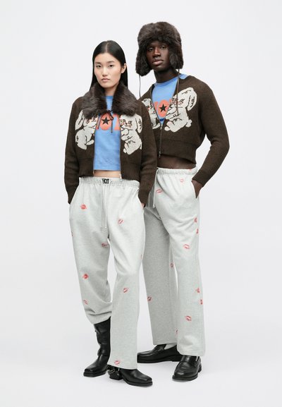 Brun stickad kofta med pälskrage, ljusblå skjorta, gråa mjukisbyxor med läpptryck, svarta stövlar och pälsfodrad hatt.