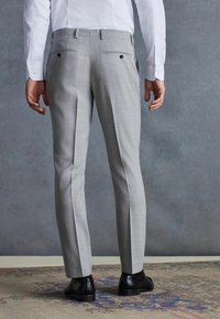 Helle graue, maßgeschneiderte Hose mit einer glatten Textur, zwei Gesäßtaschen und geradem Schnitt. Kombiniert mit schwarzen Lederschuhen.