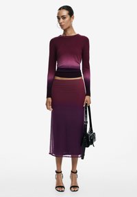 Maglione a maniche lunghe in gradiente e gonna coordinata in tonalità di viola profondo, con una silhouette fit e tessuto trasparente. Borsa nera e tacchi a strappo.
