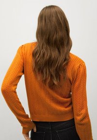 Pomarańczowy sweter dzianinowy z teksturowanym wzorem w rybą, z długimi rękawami i dopasowaną talią. Widok z tyłu.