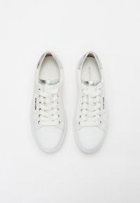 Białe skórzane sneakersy o gładkiej fakturze, z metalicznymi akcentami wokół kołnierza oraz sześcioma parami oczek na sznurówki.