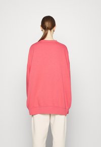 Överdimensionerad rosa sweatshirt med rund hals, sänkta axlar och ribbade manschetter, stylad med krämfärgade byxor. Slät textur.