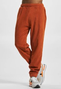 Orange fleece joggers with an elastic waistband, featuring side pockets and a tapered leg design, paired with grey and orange sneakers.