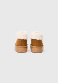 Brune ruskindsankle støvler med fluffy hvide manchetter og en tekstureret beige sål. Har en glat finish og rund tådesign.