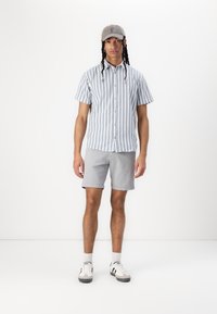 Chemise à manches courtes à rayures bleues claires et blanches, assortie à un short gris et une casquette grise. Les chaussures présentent des accents noirs et blancs.