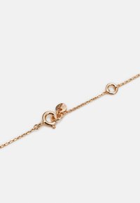 Pulseira de corrente dourada com um fecho com um laço decorativo e uma pequena etiqueta de logotipo, destacando um design de elos fino e um acabamento polido.