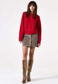 Rood geribbelde trui met halve rits, beige knoopsluiting corduroy rok, en metallic kniehoge laarzen, die samen een gelaagd, textuurvol outfit creëren.