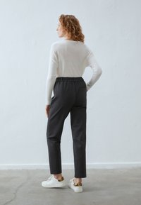 Lichtgewicht, wit langemmouwtop gecombineerd met donkergrijze tapered broek en casual witte sneakers met gouden accenten. Eenvoudig ontwerp.