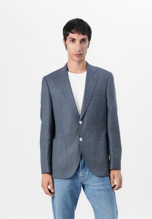 Blazer in blue check pattern with two buttons, notched lapels, and side pockets, worn over a white T-shirt and blue jeans.